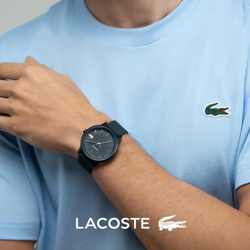Person in a light blue Lacoste T-shirt wearing a dark Lacoste watch, Lacoste logo at the bottom.