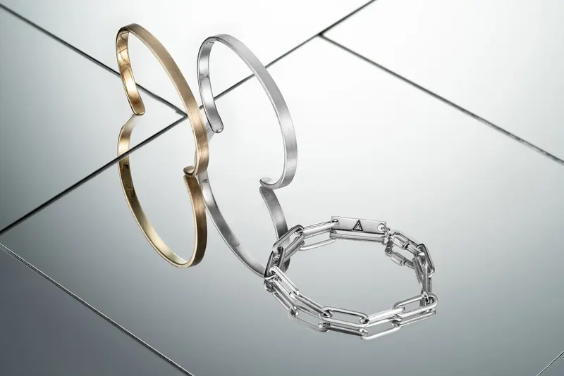 Gold and silver cuff bracelets and a silver chain bracelet on angled mirrored surfaces.