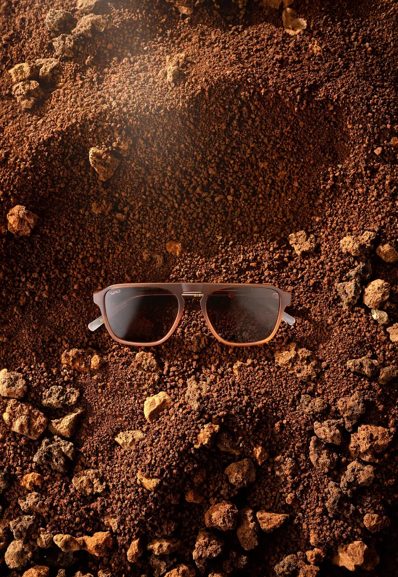 Sunglasses with brown lenses resting in red rocky soil with dust in the air.