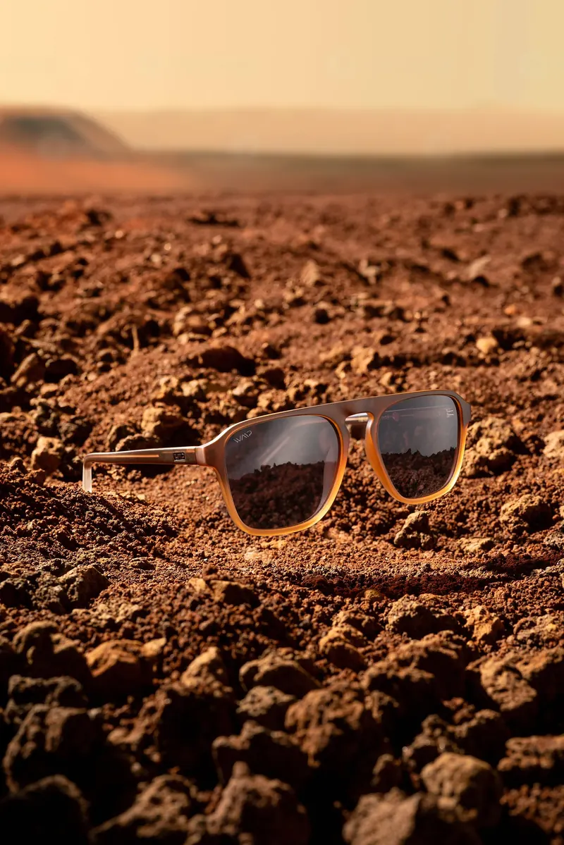 Sunglasses resting on red rocky ground with a hazy desert horizon behind.