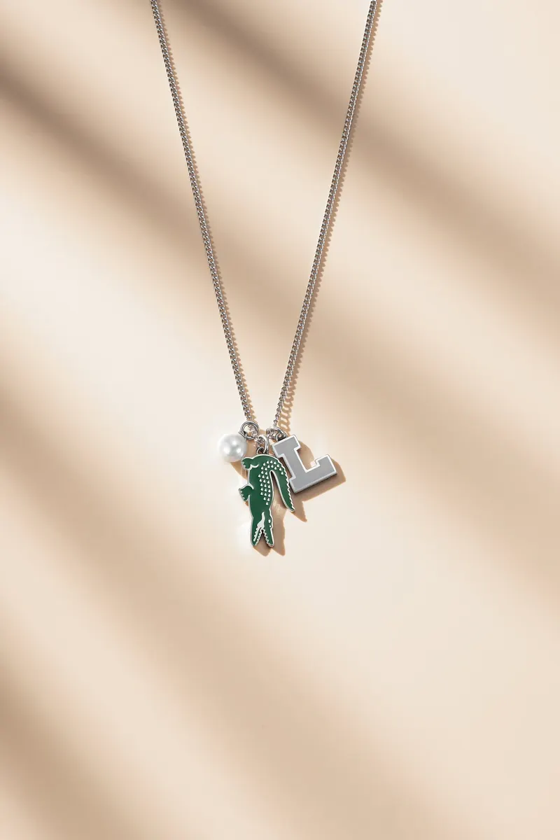 Silver chain with a green and silver crocodile pendant hanging against a cream background with soft shadows.