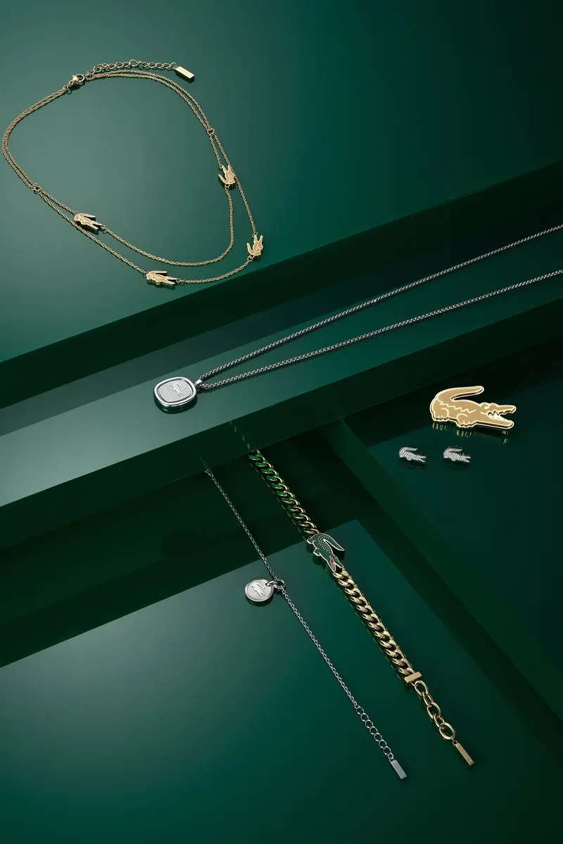 Lacoste necklaces, bracelet and crocodile studs arranged on stepped dark green surfaces.