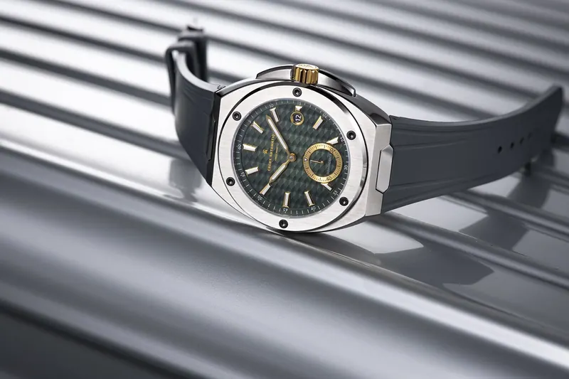 Steel watch with a green dial and black strap lying on ribbed silver metal panels.