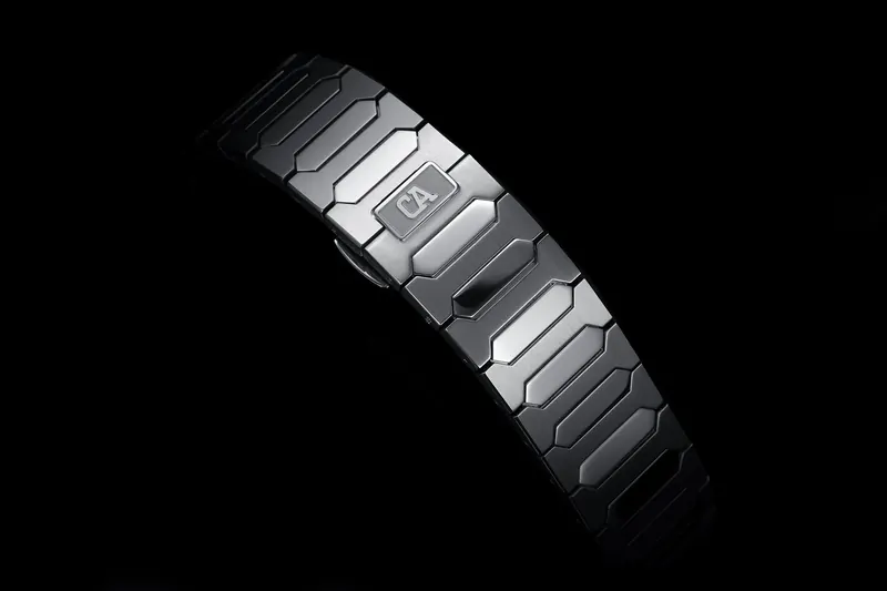 Close-up of a dark metal watch bracelet catching a hard edge light against black.