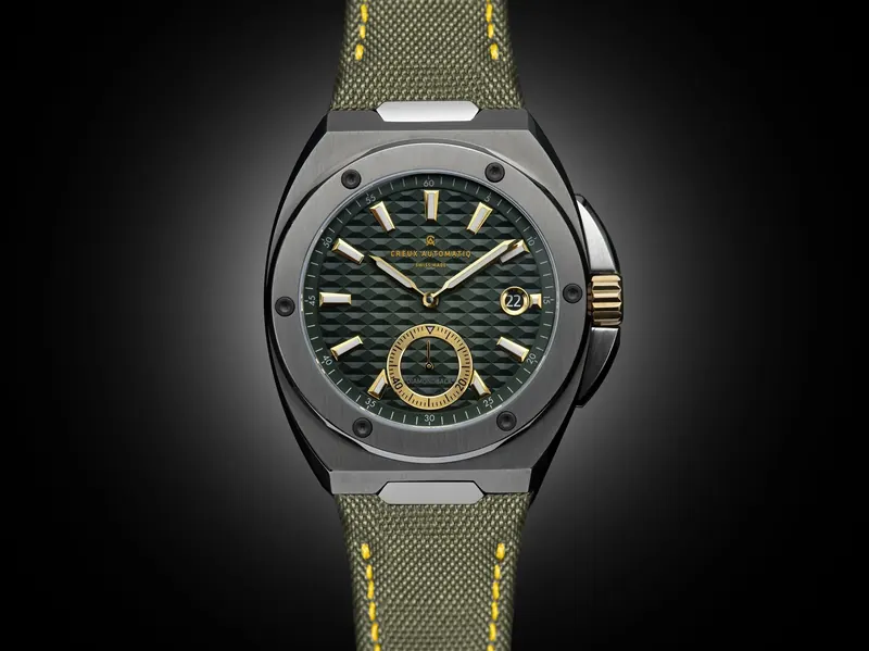 Watch with a green textured dial and olive strap with yellow stitching, spotlit on a black background.