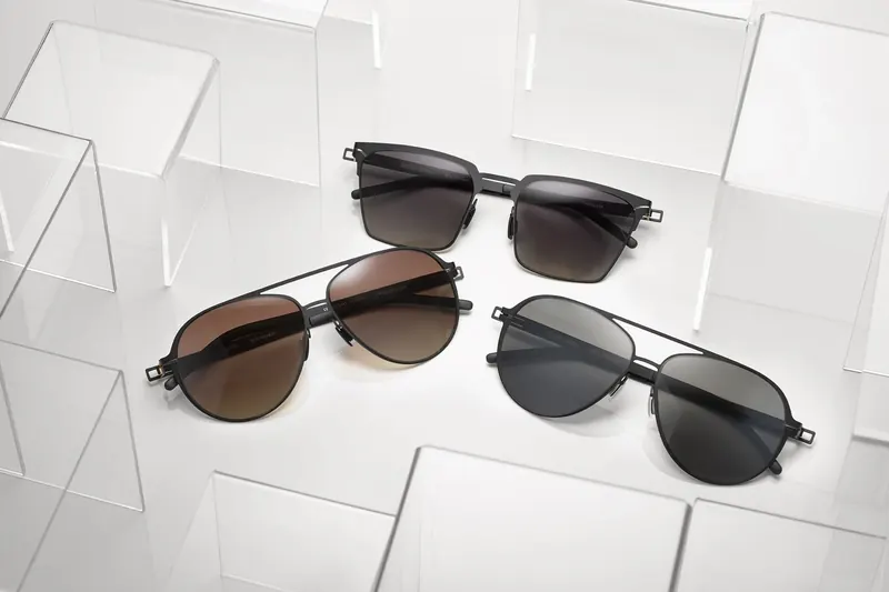 Three pairs of metal-framed sunglasses on clear acrylic blocks against white.