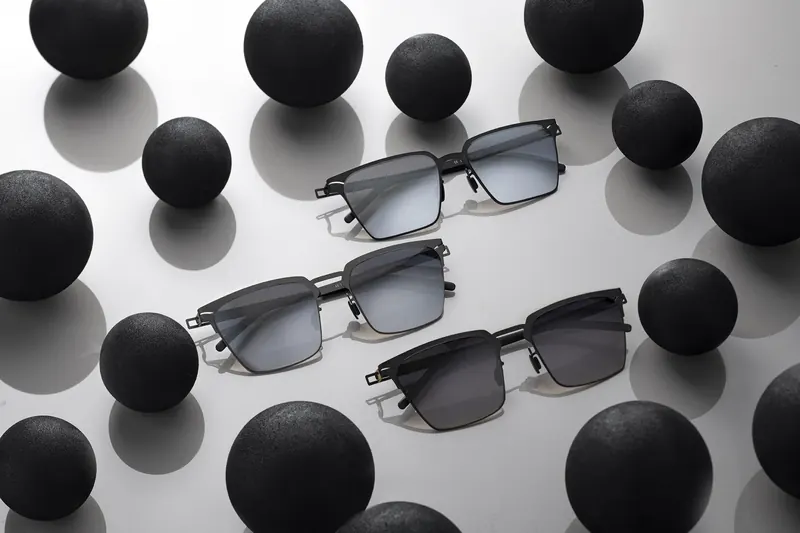 Metal-framed glasses placed among matte black spheres on a white surface.