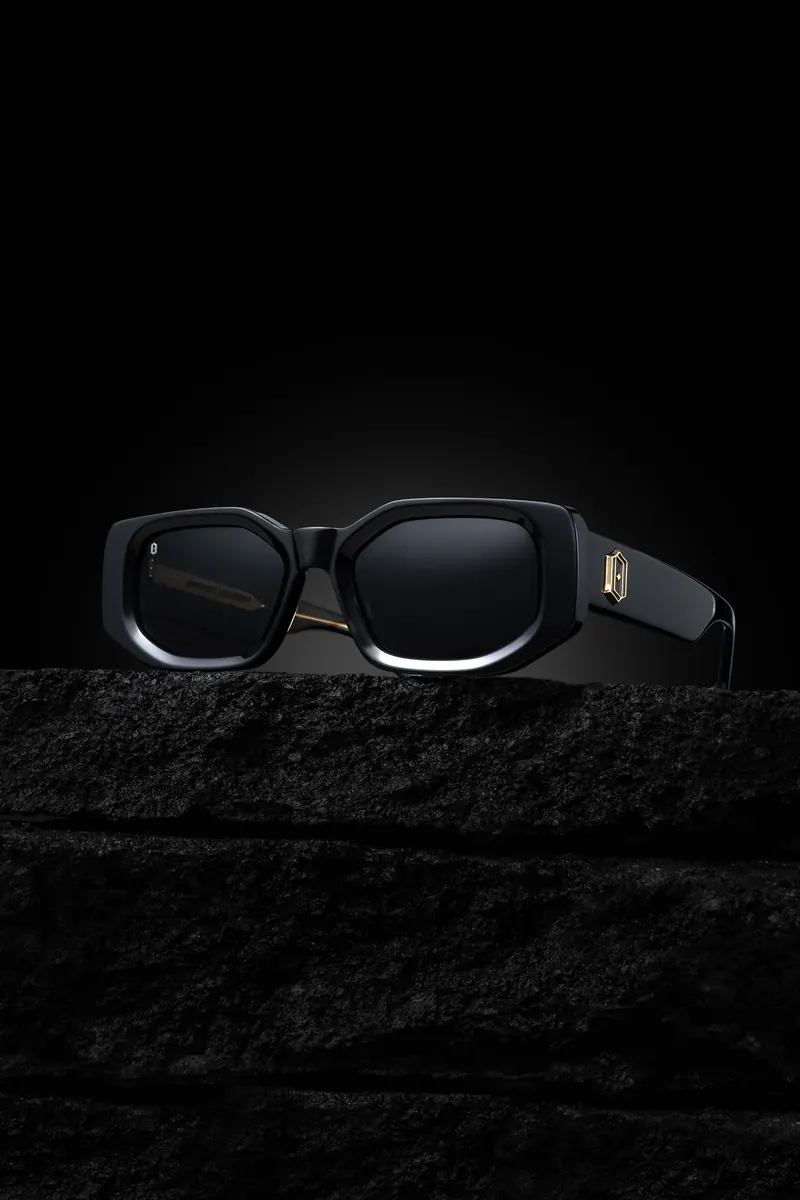 Thick black sunglasses resting on dark stone, outlined by rim light against black.