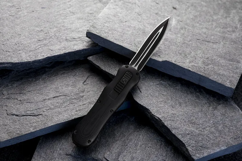 Black out-the-front knife resting on split grey slate.