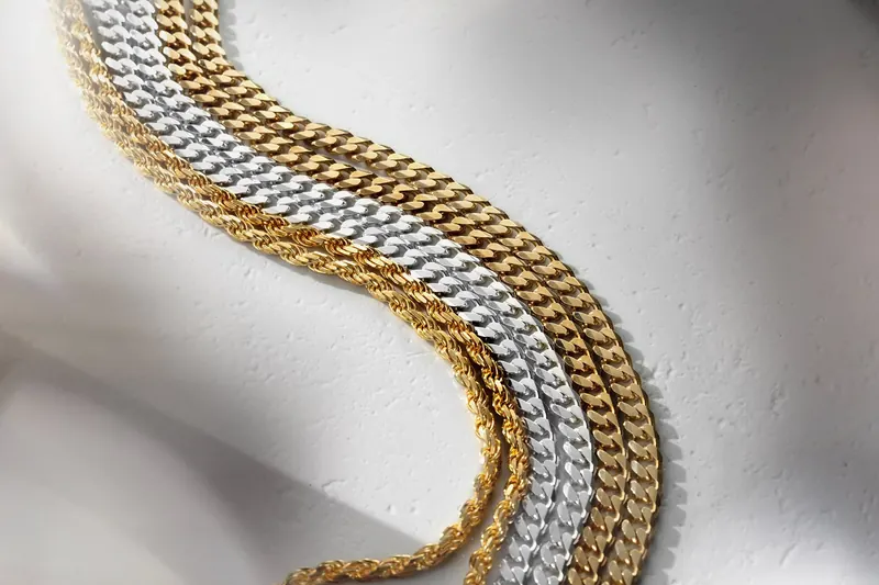 Stacked gold and silver curb chains curving across a white textured surface.