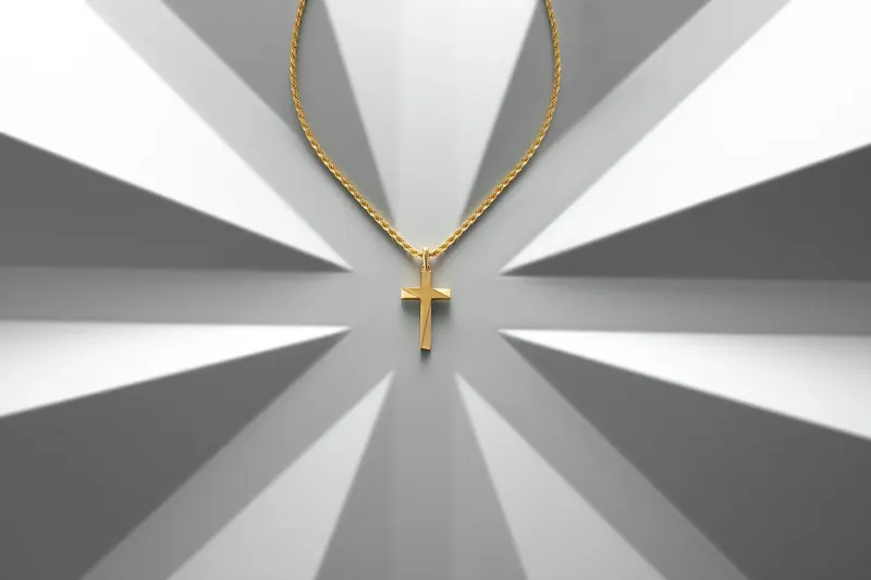 Gold chain with a small cross pendant on a grey and white sunburst-patterned background.