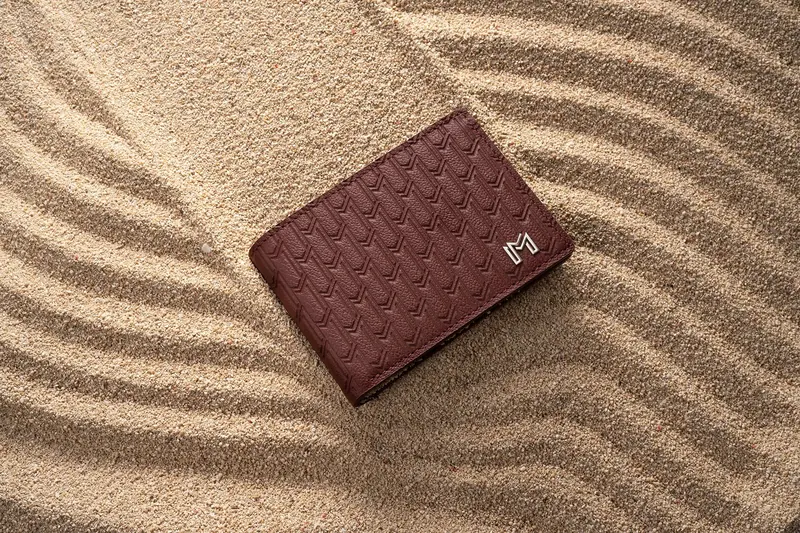 Oxblood woven-leather wallet resting on raked sand.