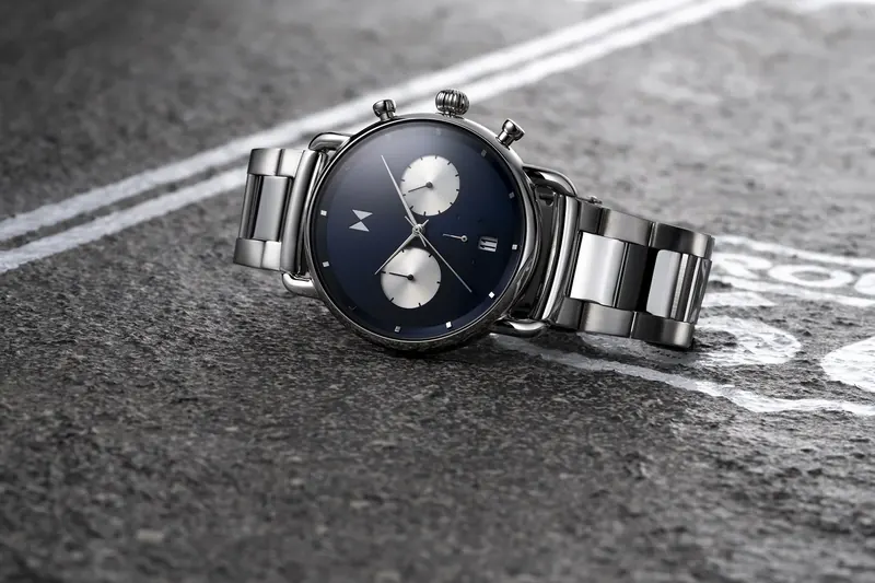 Steel MVMT chronograph with a navy dial lying on asphalt next to painted white road lines.