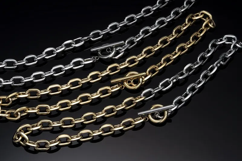 Gold and silver chain necklaces with toggle clasps arranged in curves on a black background.