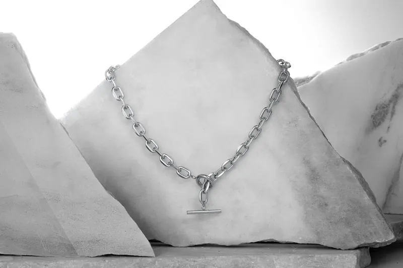 Silver chain necklace with a toggle bar draped over pale stone blocks.