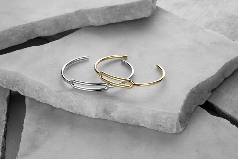 Silver and gold open cuff bracelets resting on broken pale stone slabs.