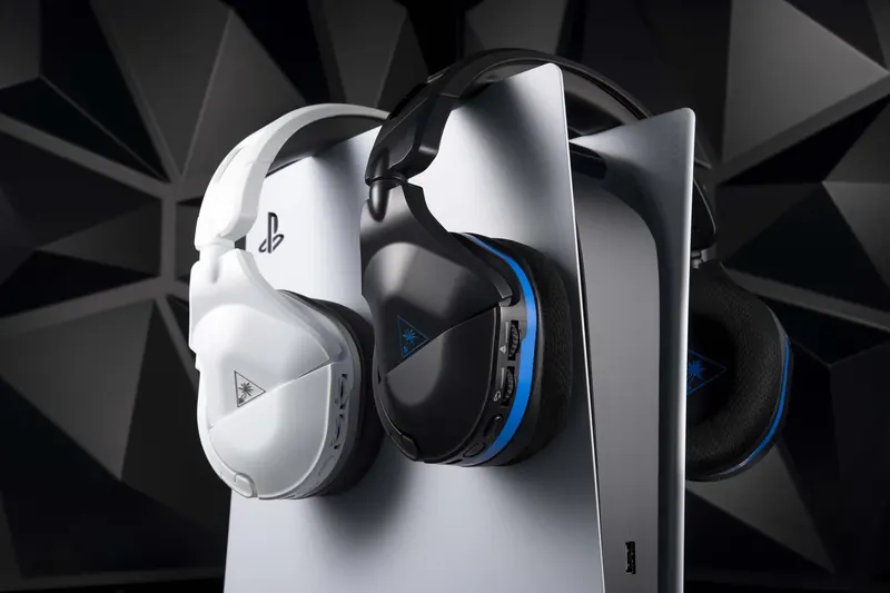 PlayStation console with three wireless gaming headsets hanging from it, two black and one white, in a soundproof room.