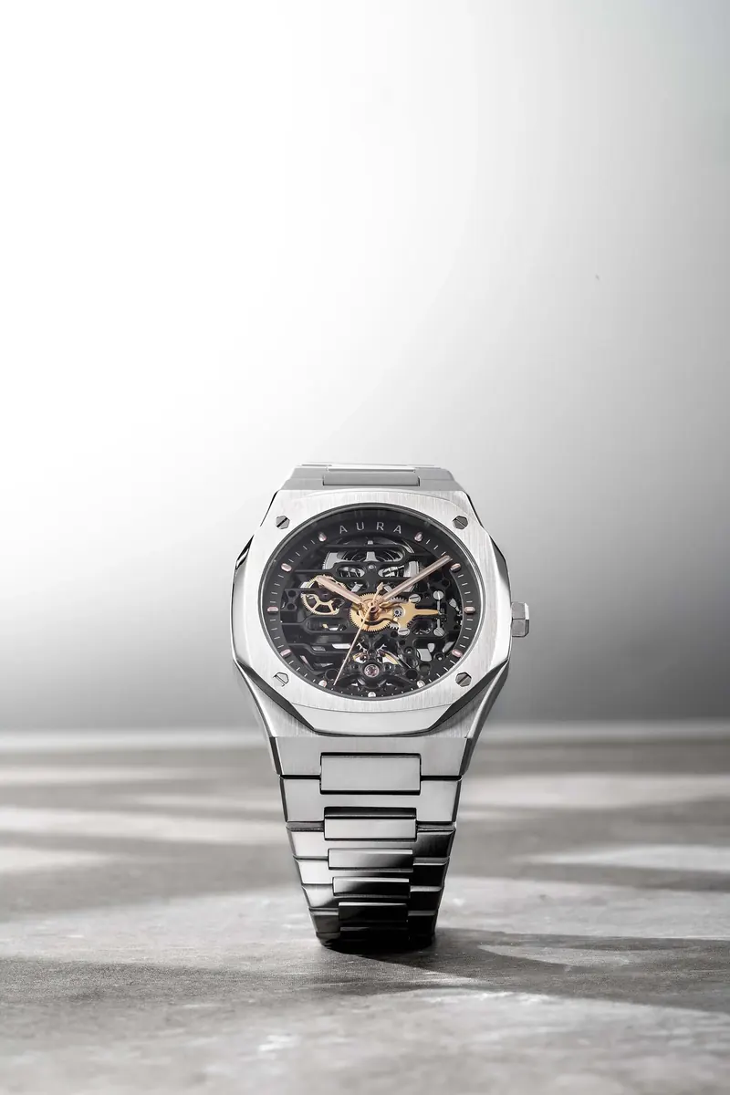 Luxury wristwatch with a metal band and black skeleton dial showing its internal mechanics, on a textured surface.