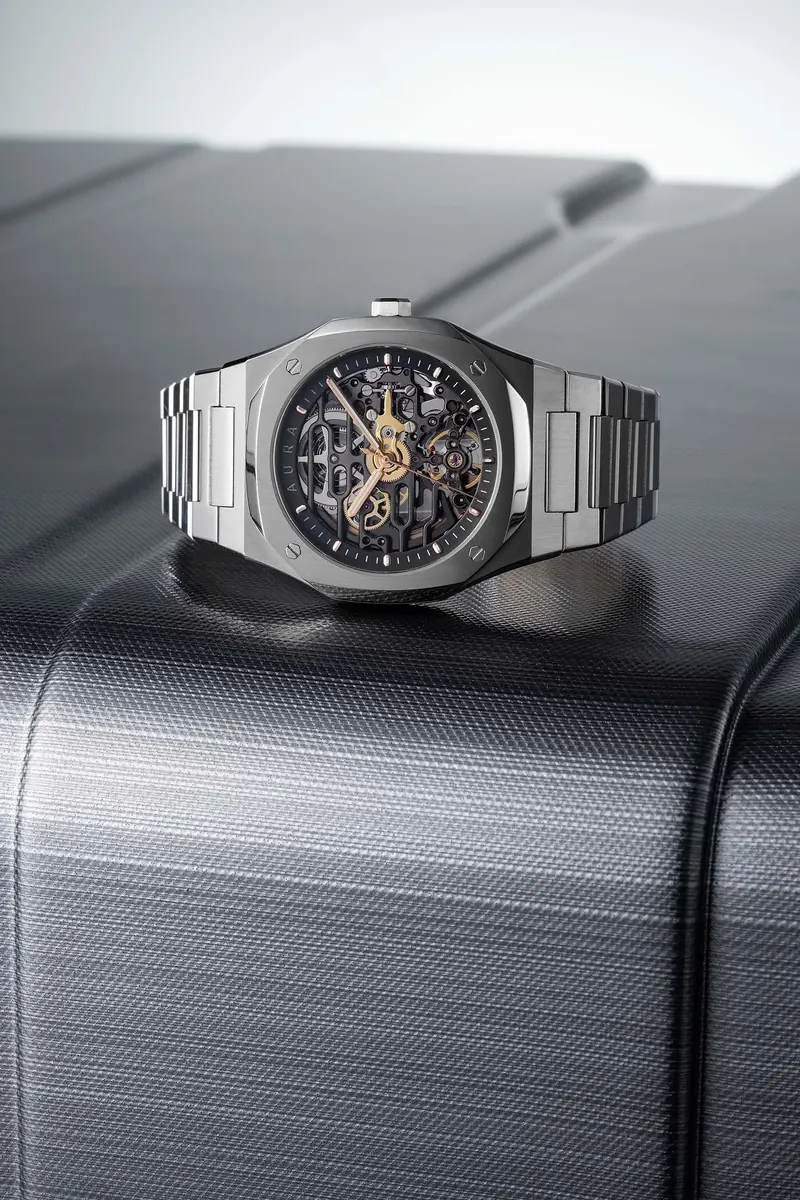 Silver skeleton watch with a metal band resting on a textured black surface.