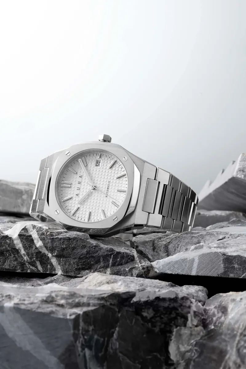 Silver wristwatch resting on grey rocks against a plain light background.