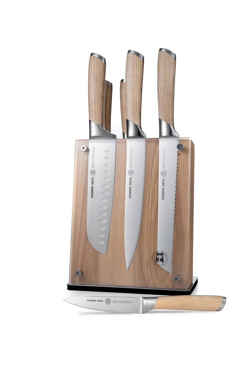 Four Schmidt Bros. kitchen knives with wooden handles on a wooden block, with one more knife lying in front.