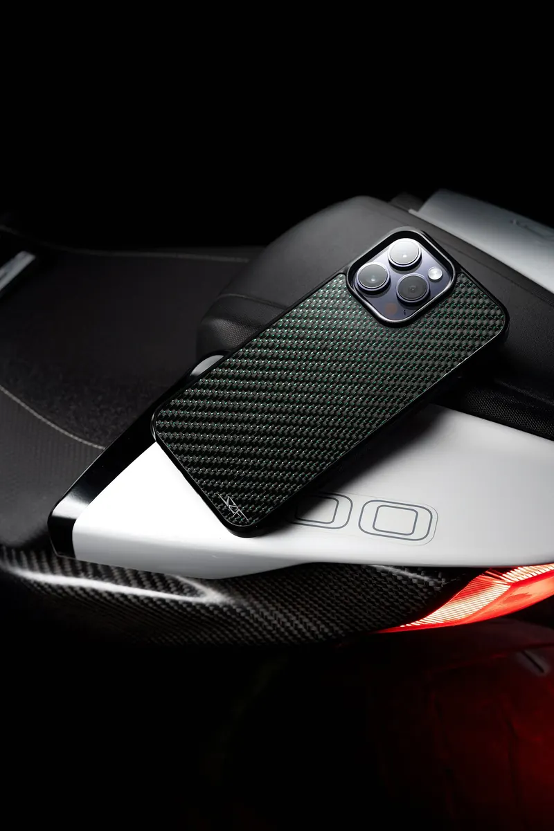Phone in a green carbon-fiber case resting on the white tail of a motorcycle.