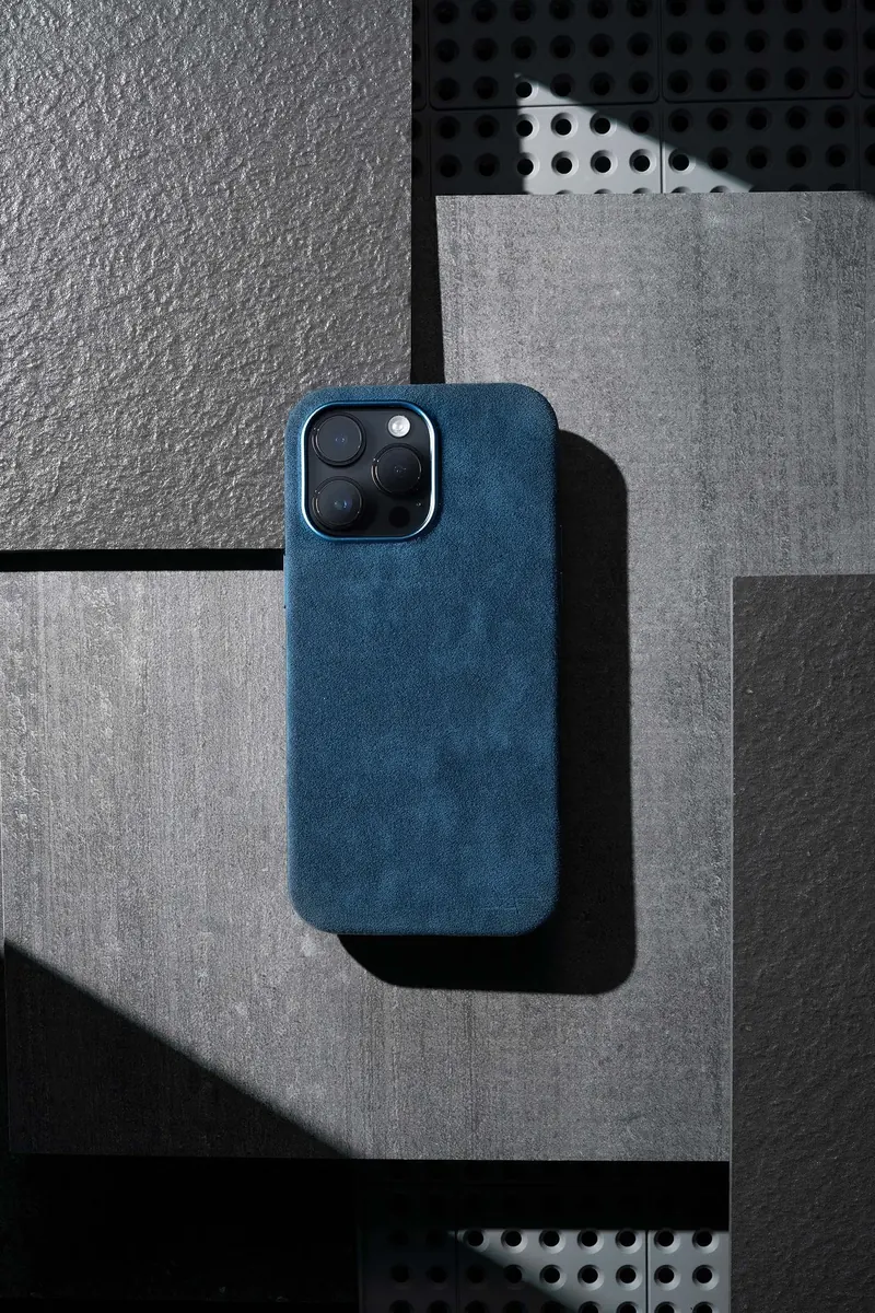Blue smartphone in a textured case resting on a geometric tiled surface with cast shadows.