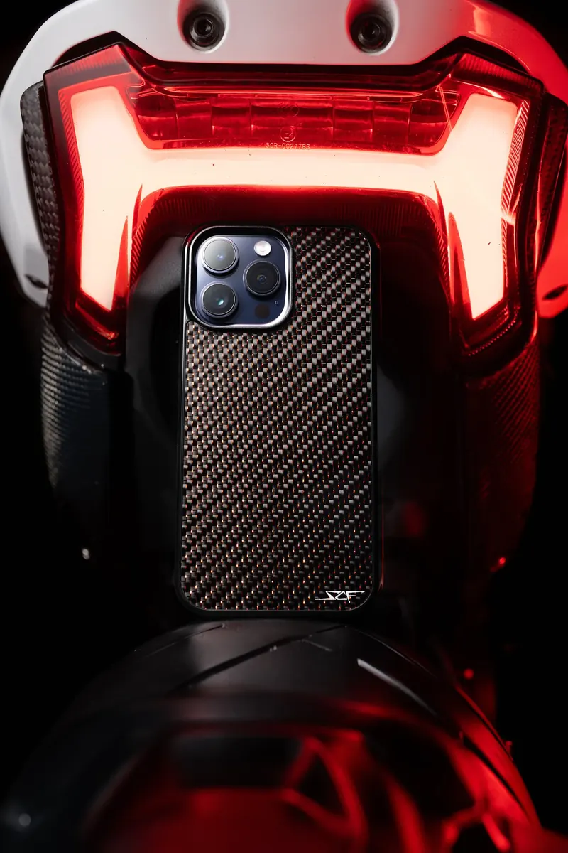 Phone in a carbon-fiber case below a glowing red motorcycle tail light.