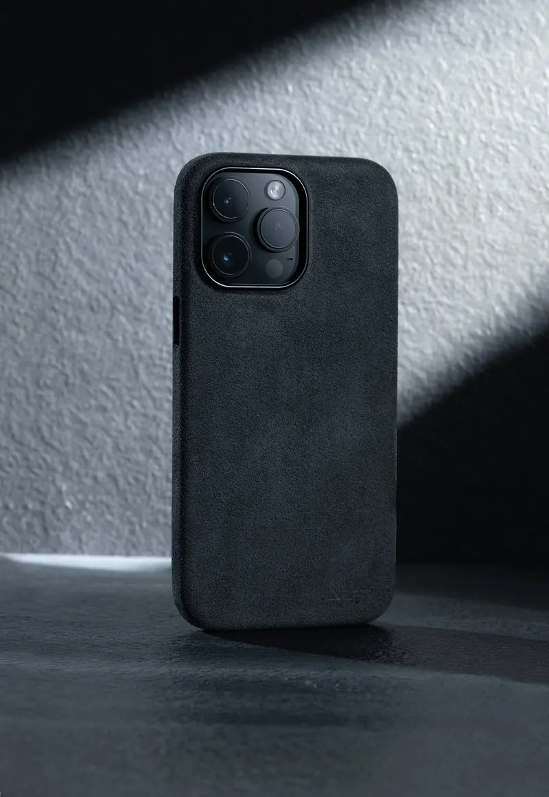 Phone in a black textured case standing in a diagonal slash of light on grey stone.
