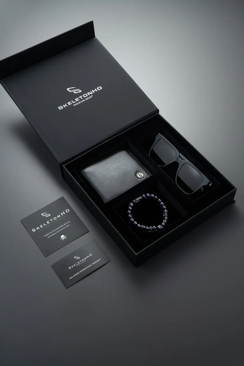 Open black Skeleton HD gift box holding a wallet, beaded bracelet and sunglasses, with cards beside it.
