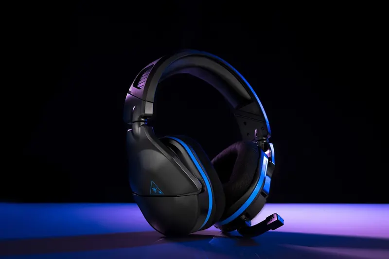 Black gaming headset on a stand lit by blue and violet LED light on black.