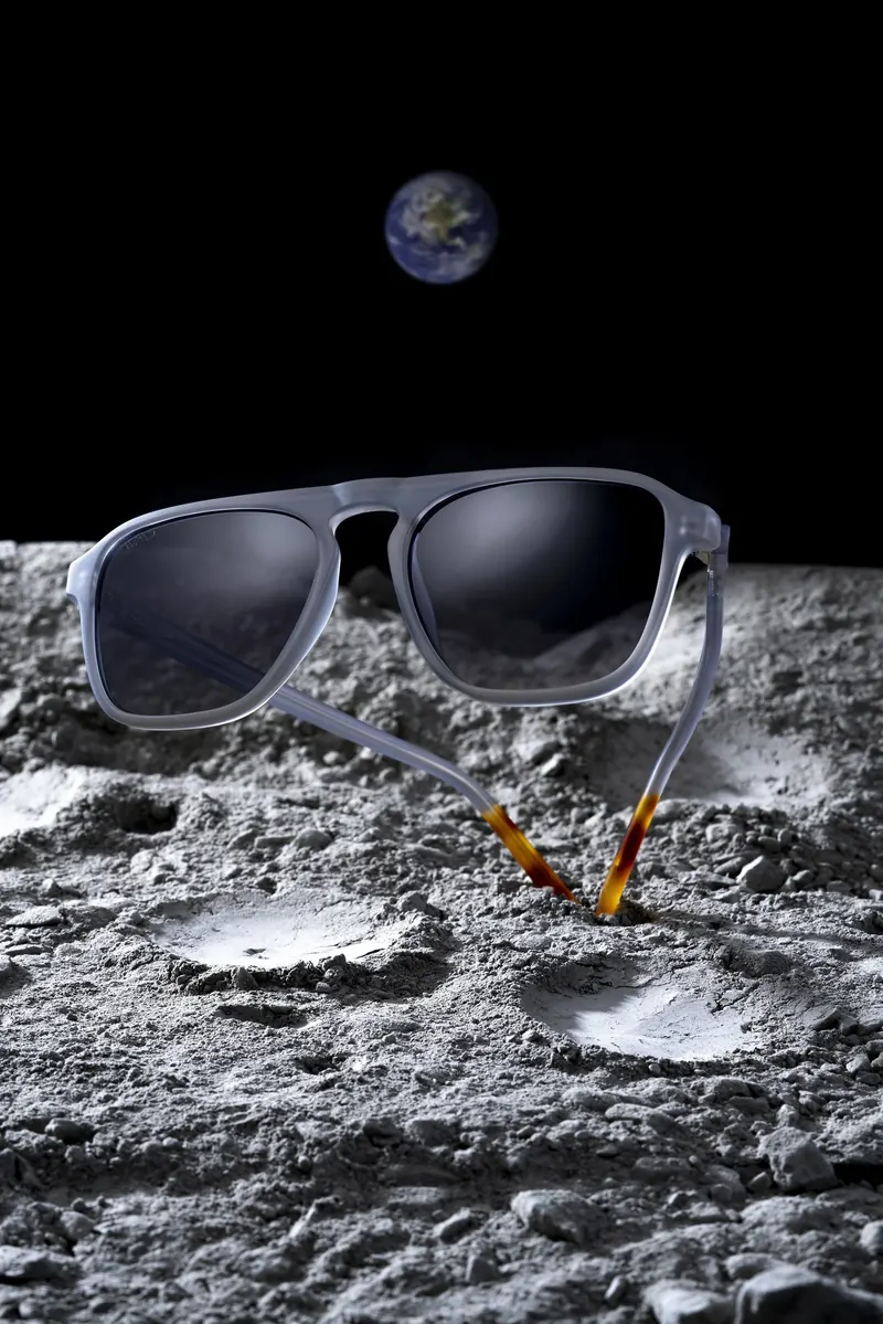 Sunglasses resting on a cratered moon-like surface with a small Earth visible in the black sky.