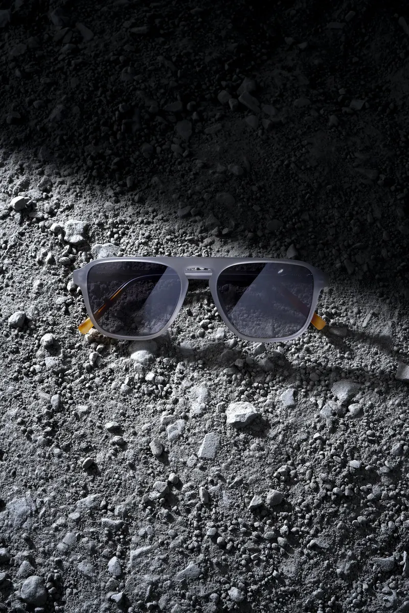 Sunglasses on grey moon-dust terrain under hard side light.