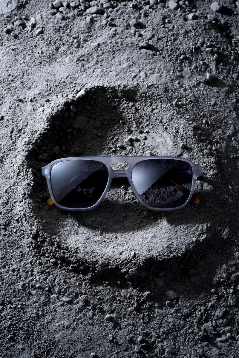 Pair of sunglasses on a moon-like surface of grey dust and rocks, casting a shadow.