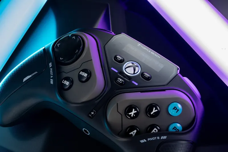 Close-up of a black game controller with extra buttons under violet and cyan light.