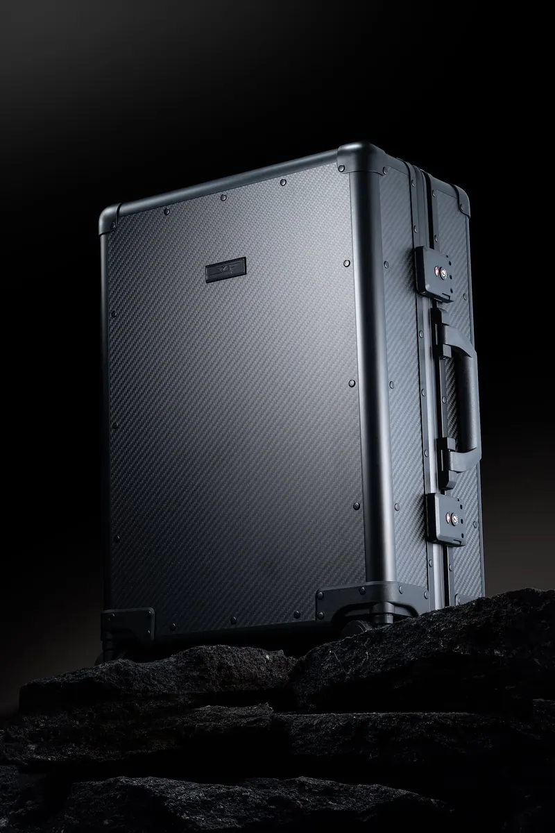 Ribbed aluminum carry-on suitcase standing on black rock under a top light.