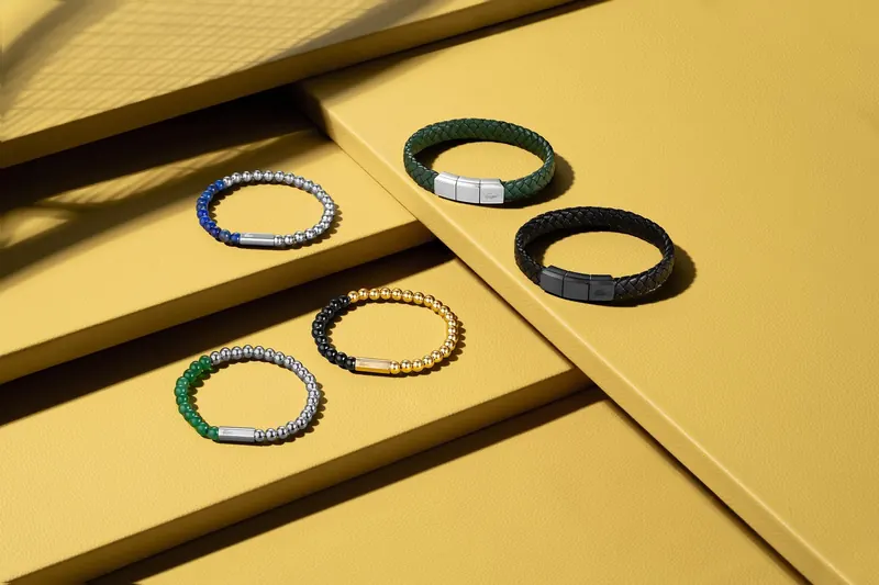 Six beaded and woven bracelets with metallic accents on stepped yellow surfaces, arranged in two rows.